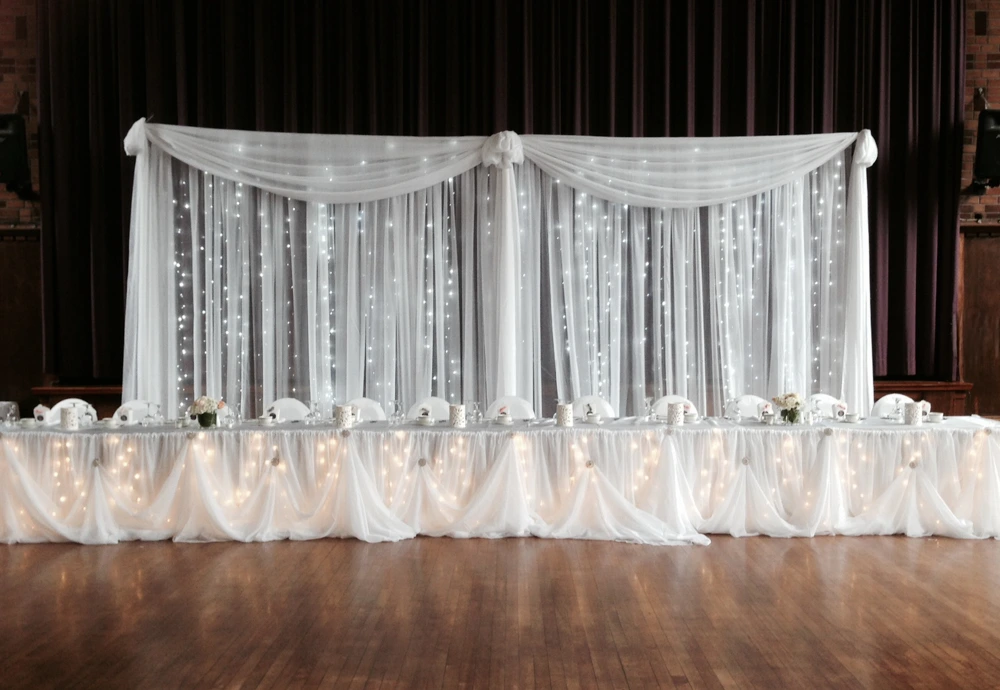 white organza head table with draping,  organza backdrop, and mini lights